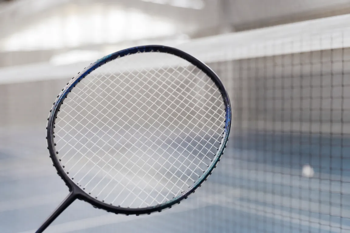 Badmintonracketshuvud i profil mot ett nät i en inomhushall