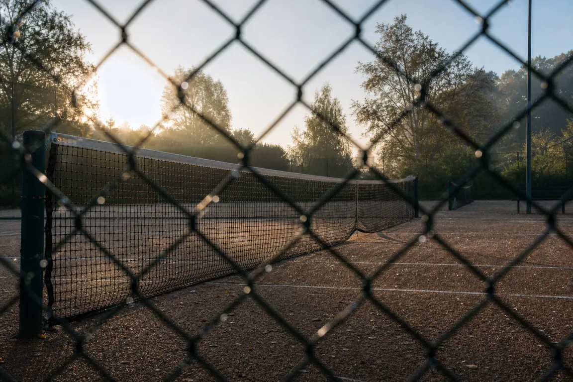 Tom grusbana för tennis sedd genom staketet i morgonljus