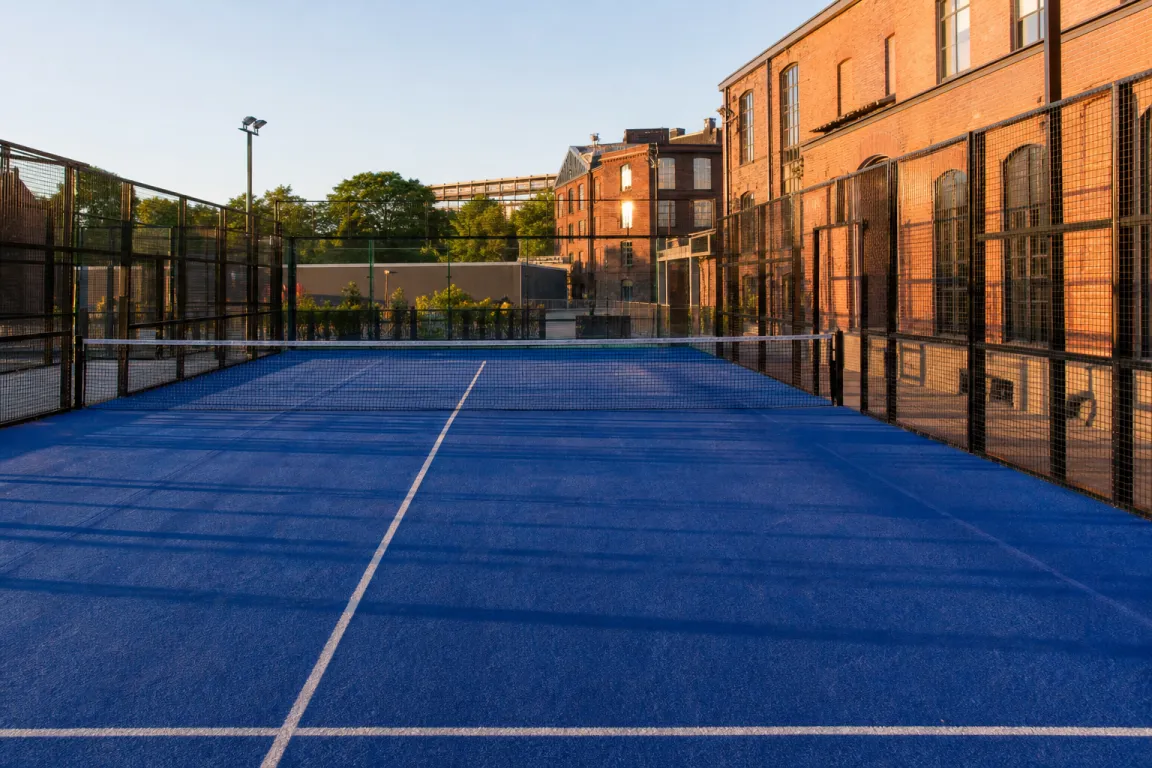 Utomhus padelbana med tegelfasad i bakgrunden i kvällssol