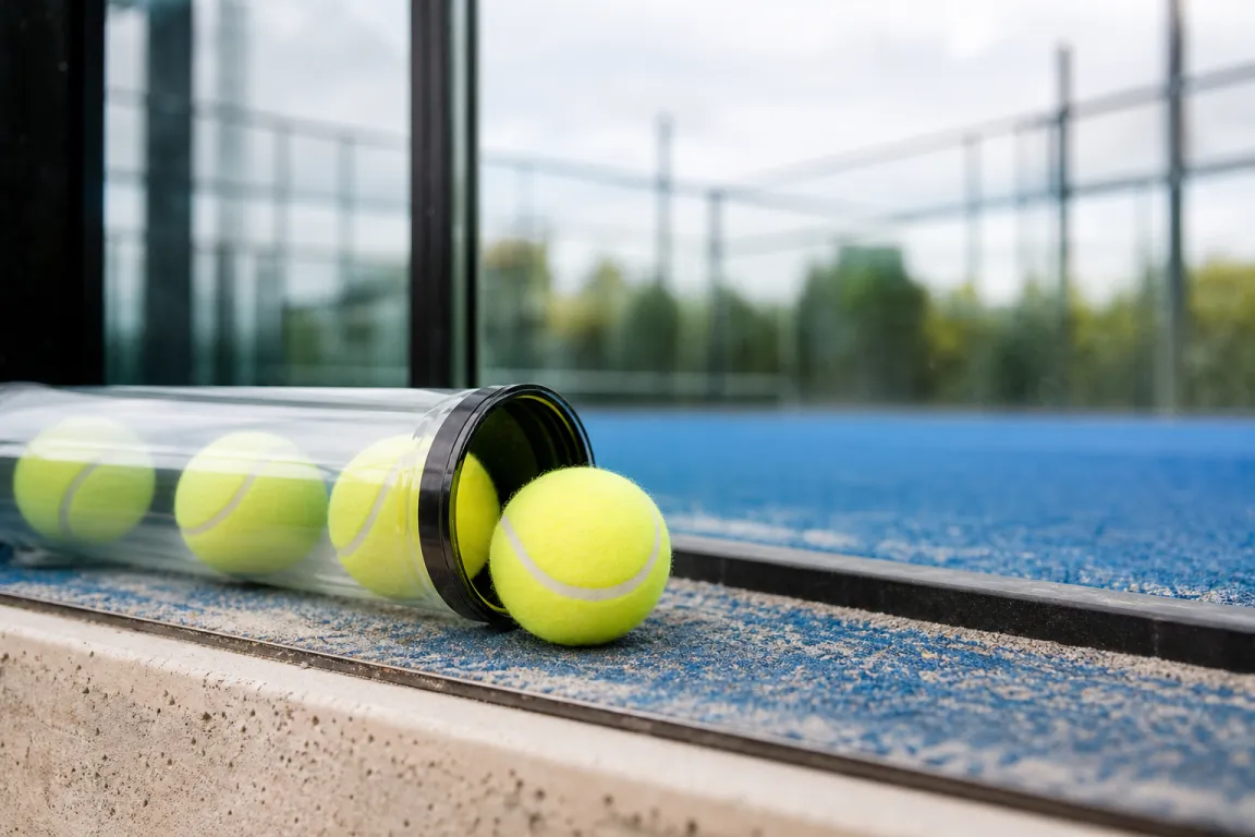 Padelbollar i ett öppet bollrör på kanten av en padelbana