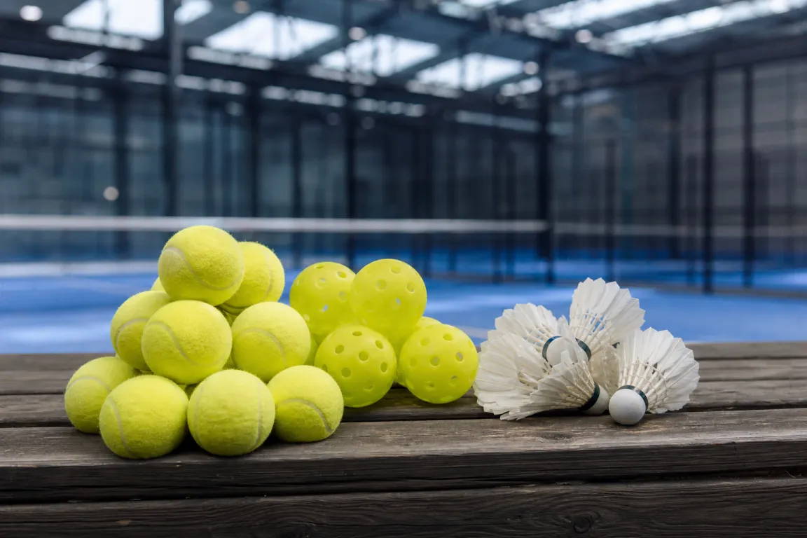 Padelbollar, tennisbollar och fjäderbollar samlade på ett bord i en sporthall
