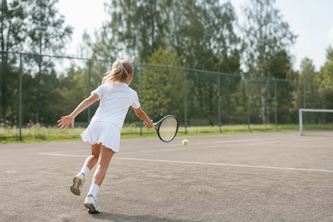 Barn i tenniskläder springer mot en boll på en mindre tennisbana