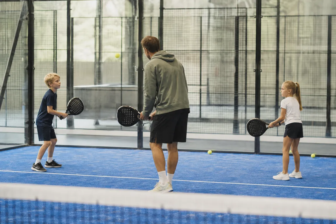 En ledare och två barn som övar grundslag på en padelbana