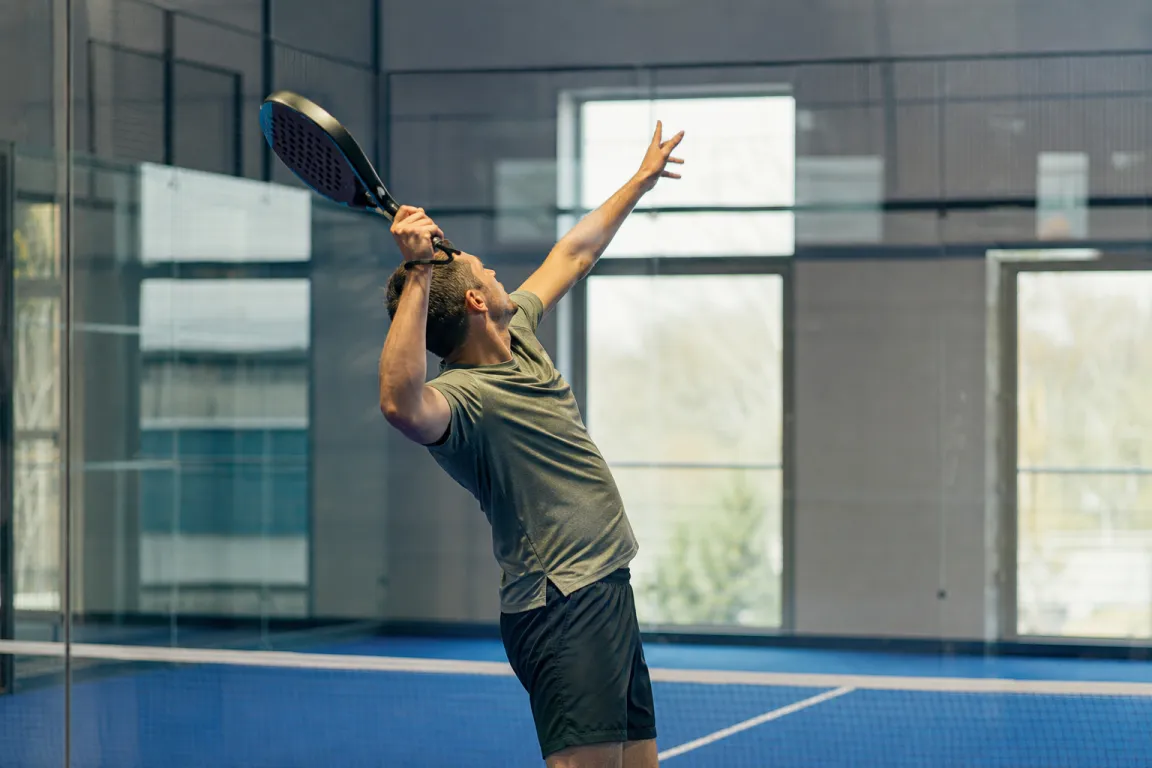 En padelspelare mitt i ett overheadslag med racket högt över huvudet