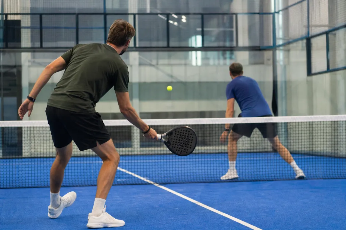 Två padelspelare mitt i en poängväxling nära nätet på en bana med glasväggar