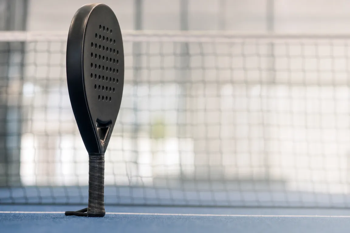 Padelracket sett i profil mot en padelbanas nät
