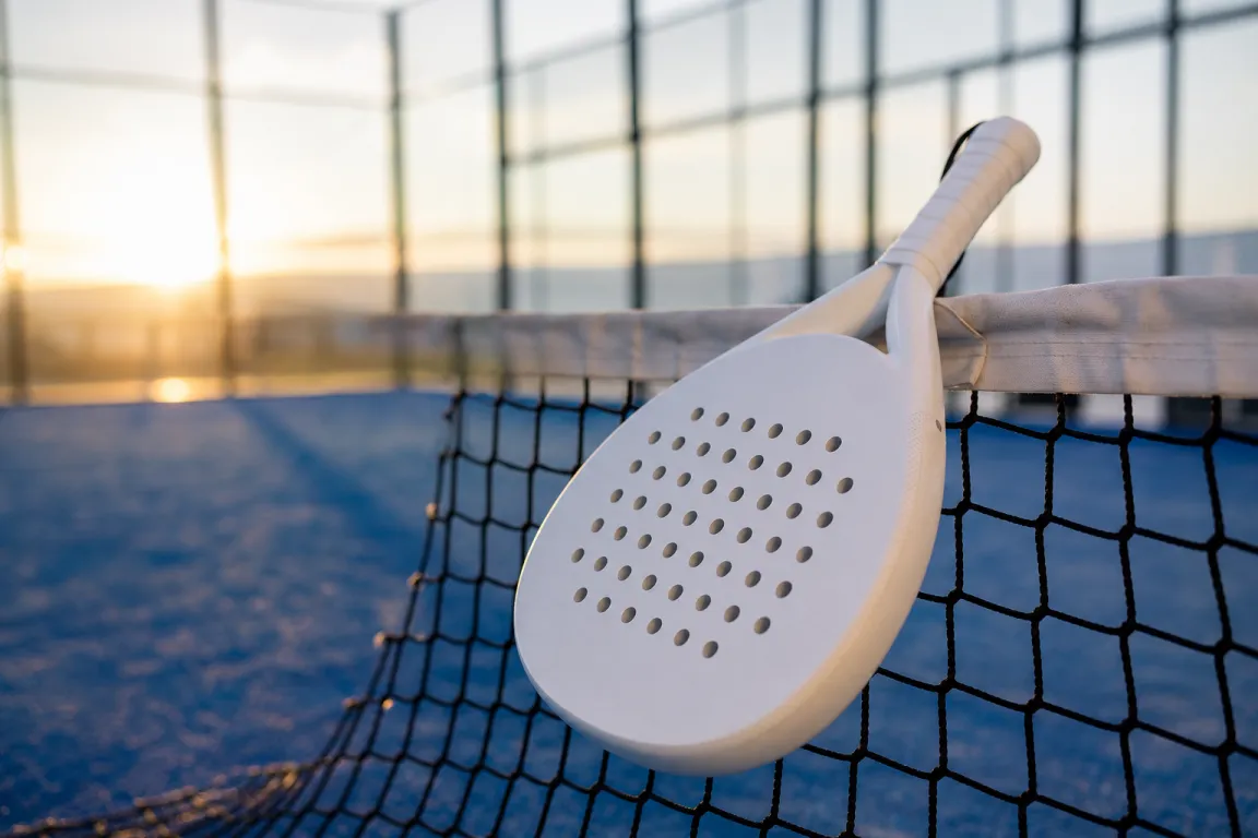 Padelracket som vilar mot nätet på en padelbana