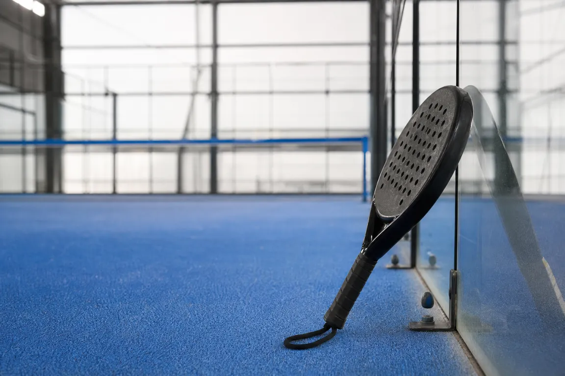 Padelracket lutad mot en padelbanas glasvägg