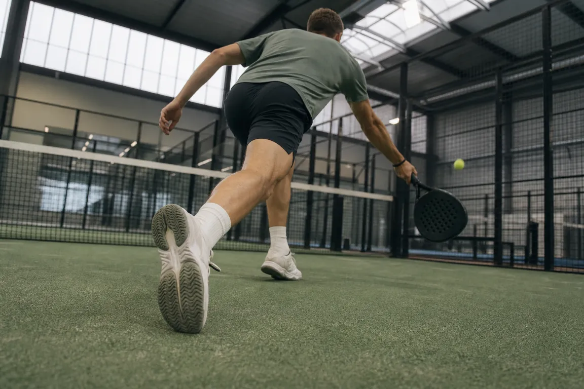 Padelspelare i utfall mot nätet med fokus på skorna