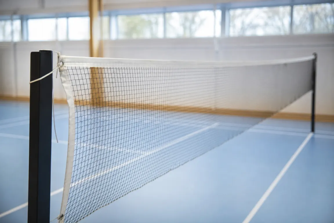 Ett spänt badmintonnät mellan två stolpar sett från sidan i en tom sporthall