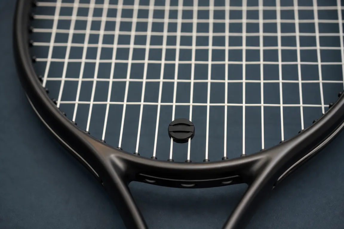 Närbild på ett tennisrackets strängar med en vibrationsdämpare monterad längst ned mot ramen